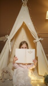 a girl holding a book while in an indoor tent
