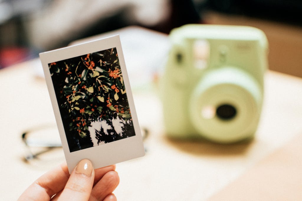 Hand holding an Instax photo of orange berries with blurred instant camera in the background.
